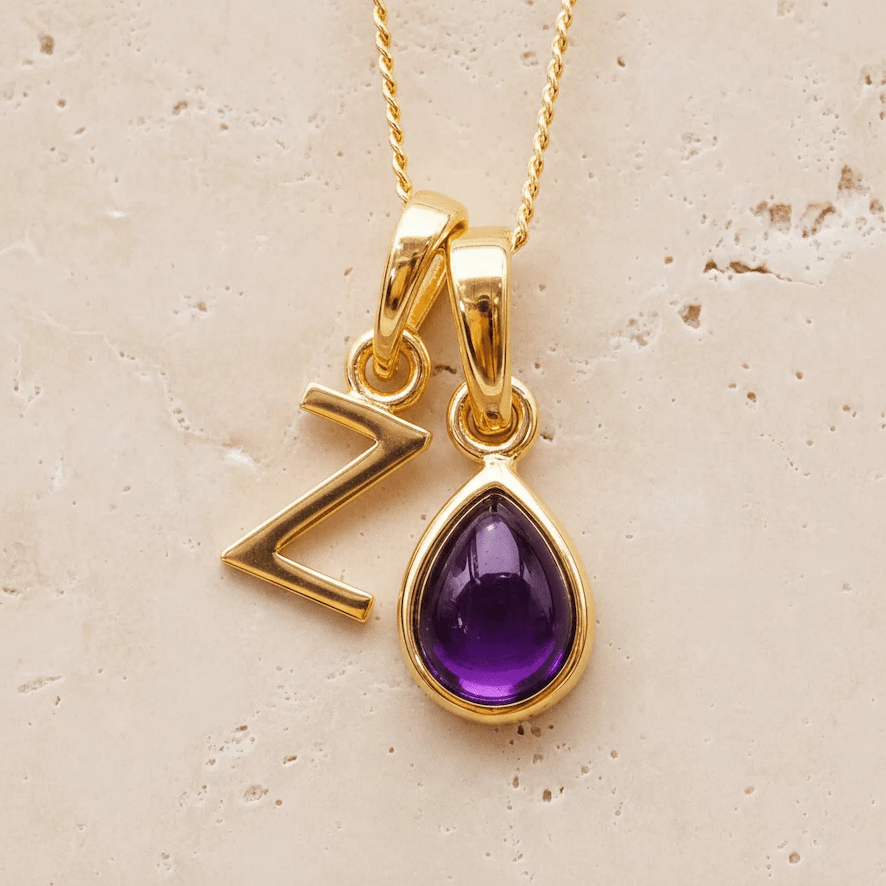 Gold double pendant necklace with a february birthstone purple teardrop amethyst gemstone pendant and letter 'Z' charm on a beige background