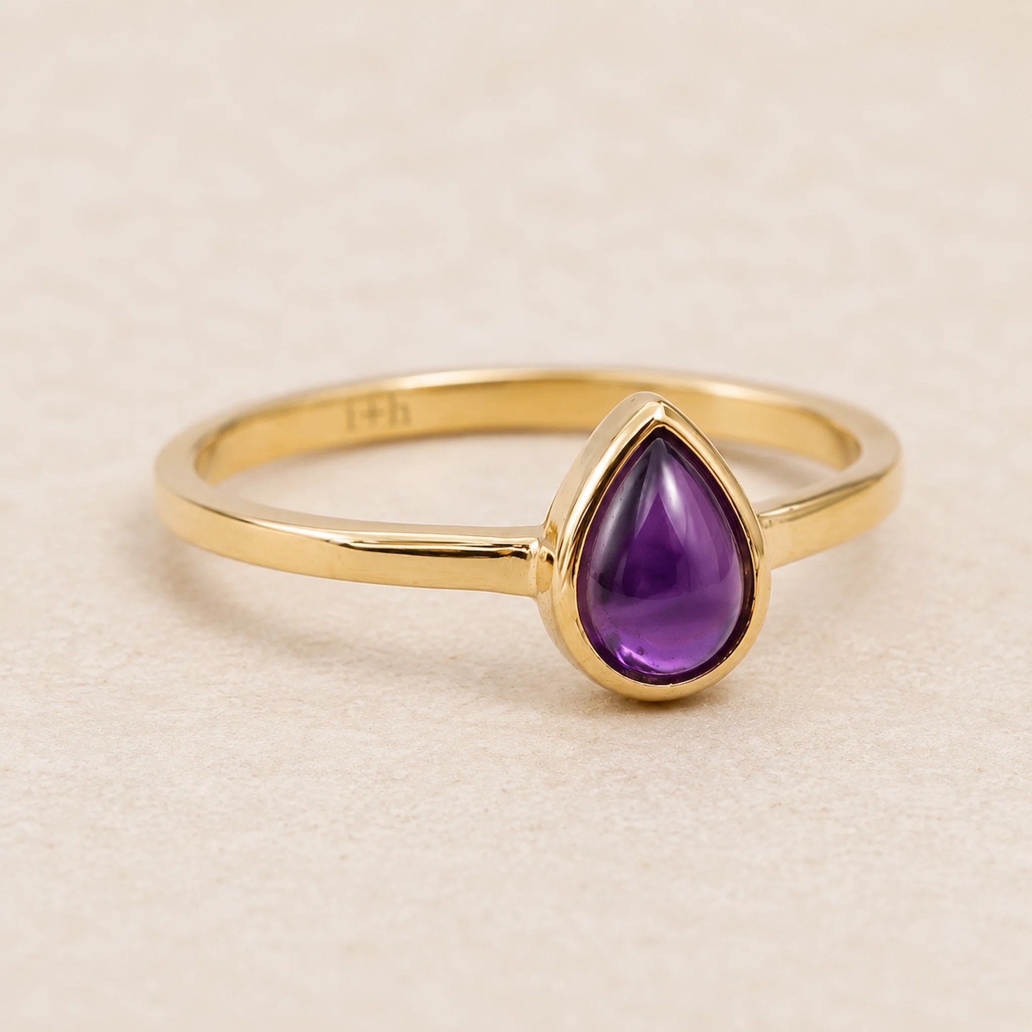 gold february birthstone pear shaped natural amethyst gemstone ring on a light background.