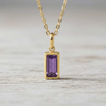 Gold necklace with a purple gemstone pendant on a white background