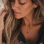 close up of a woman wearing gold february birthstone jewellery set including a dainty gold amethyst pendant necklace and matching amethyst stud earrings