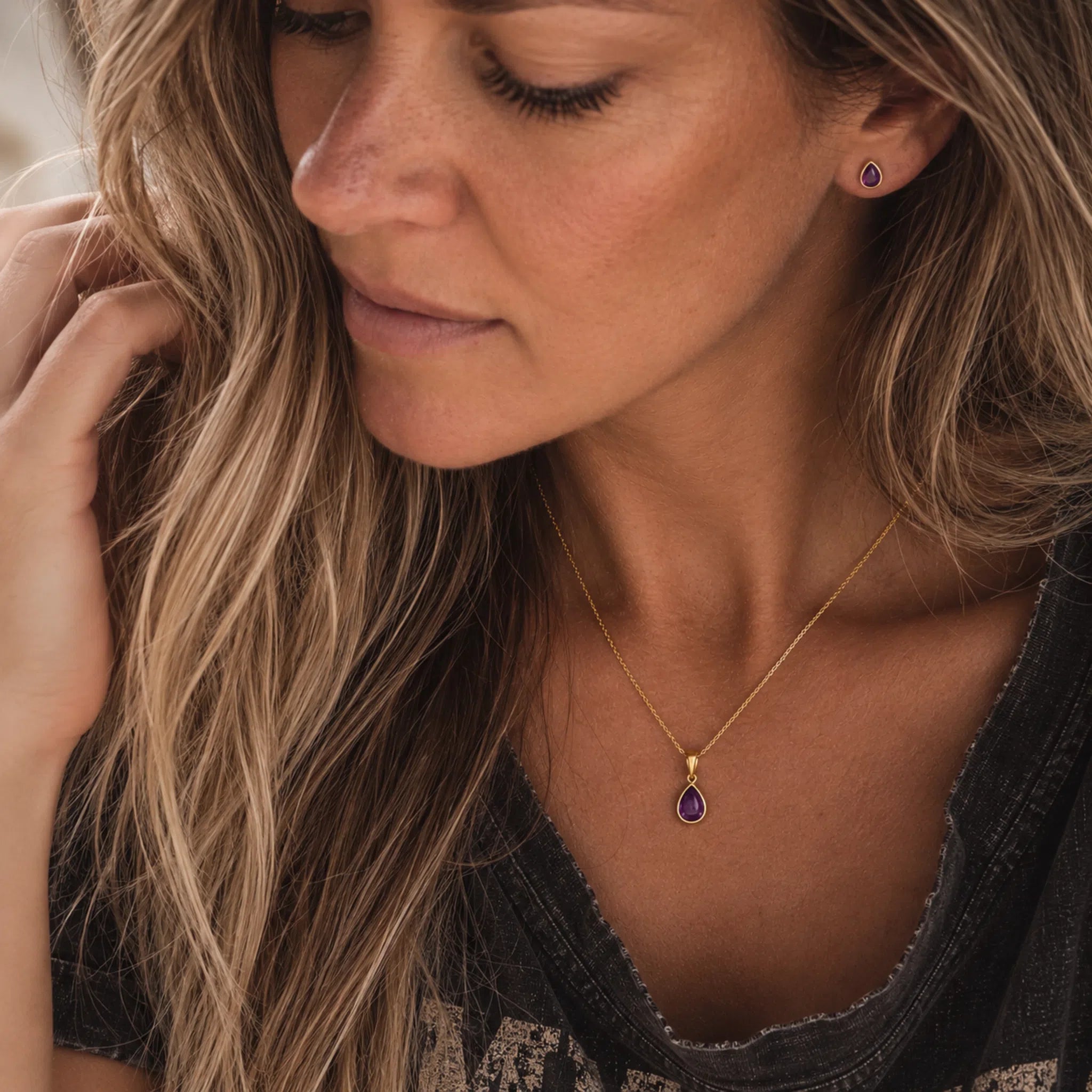 close up of a woman wearing gold february birthstone jewellery set including a dainty gold amethyst pendant necklace and matching amethyst stud earrings
