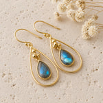 pair of gold french hook earrings with natural faceted labradorite gemstones on a light stone surface 