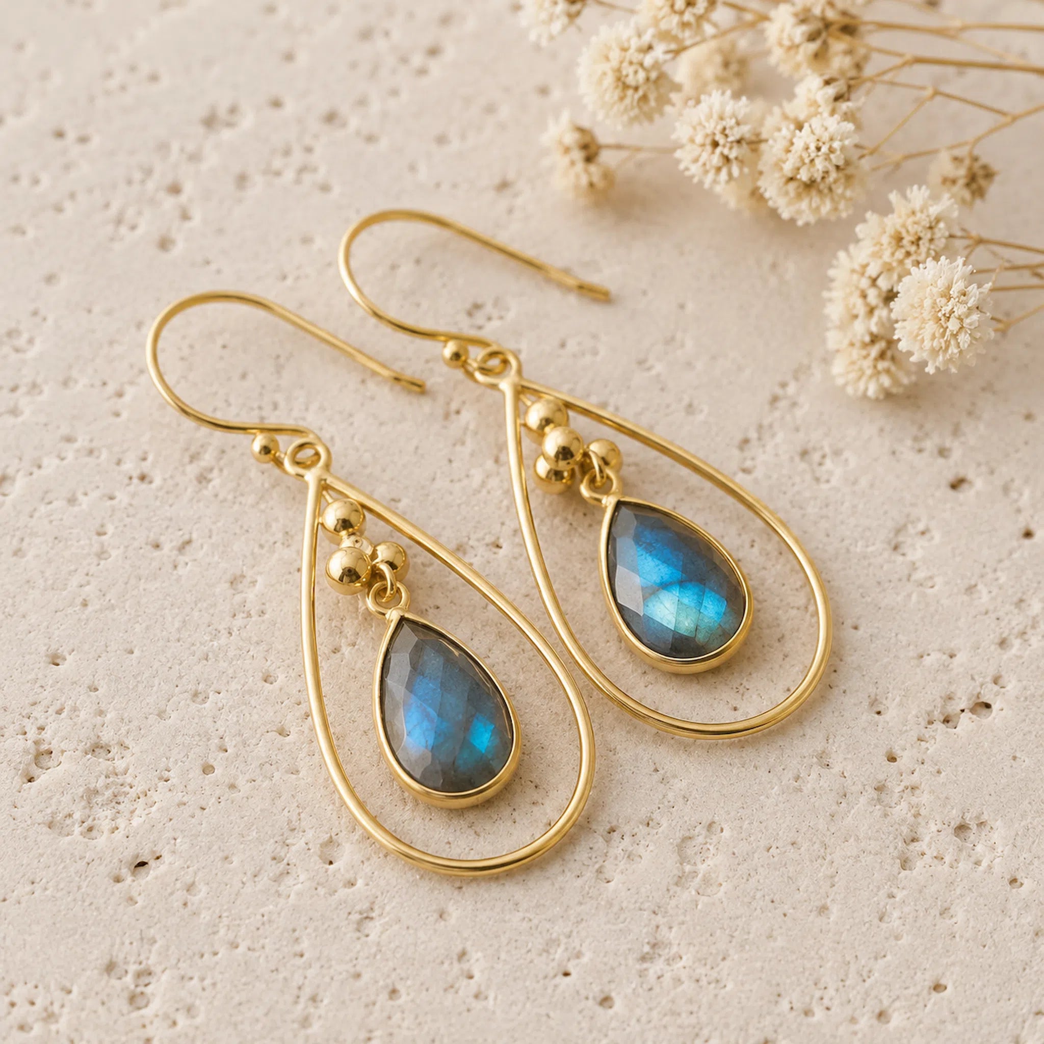 pair of gold french hook earrings with natural faceted labradorite gemstones on a light stone surface 