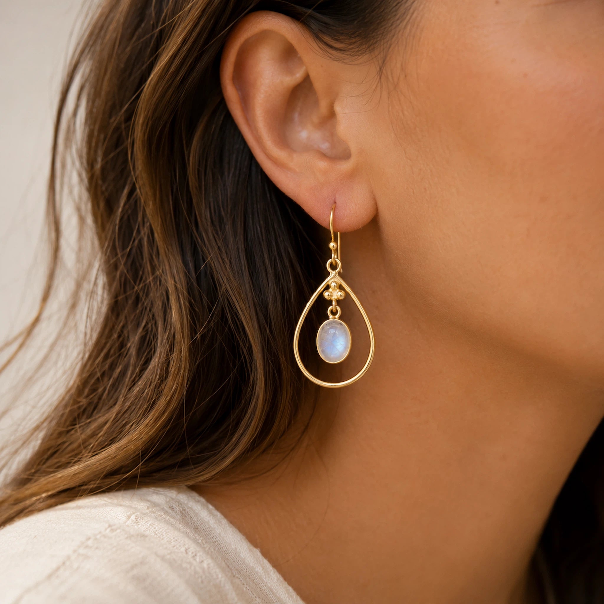 close up of a woman wearing gold french hook earrings with bezel set natural cabochon moonstone