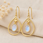 pair of gold french hook earrings with bezel set natural cabochon moonstones on a textured fabric