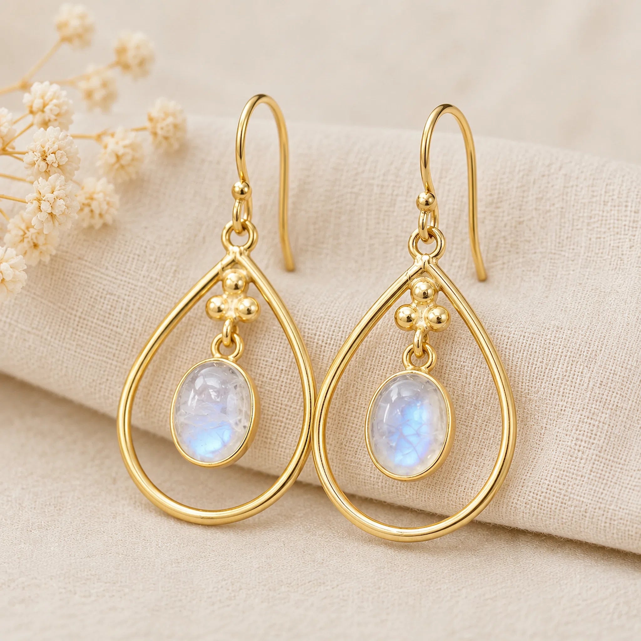 pair of gold french hook earrings with bezel set natural cabochon moonstones on a textured fabric