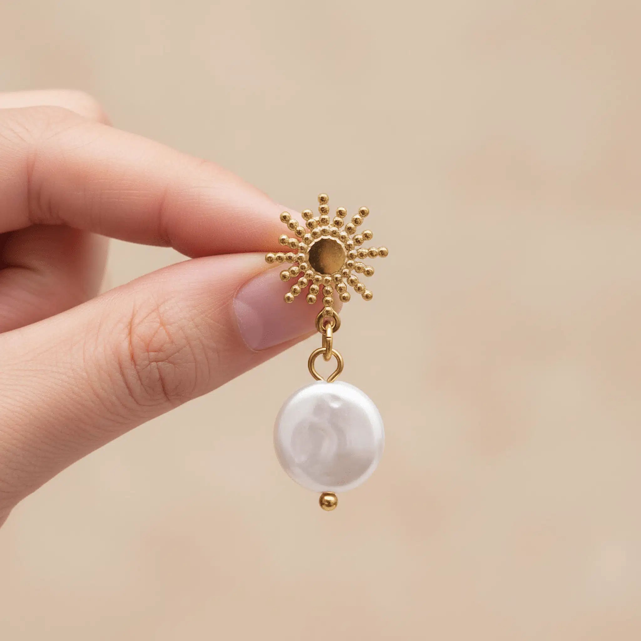 gold starburst sun shaped stud pearl earring with natural freshwater pearl being held by fingers