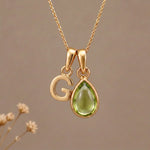 Gold Initial G Pendant and August birthstone Natural Peridot Necklace against a warm background