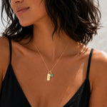 Gold gemini line glyph pendant and teardrop may birthstone natural emerald pendant necklace on a person wearing a singlet.