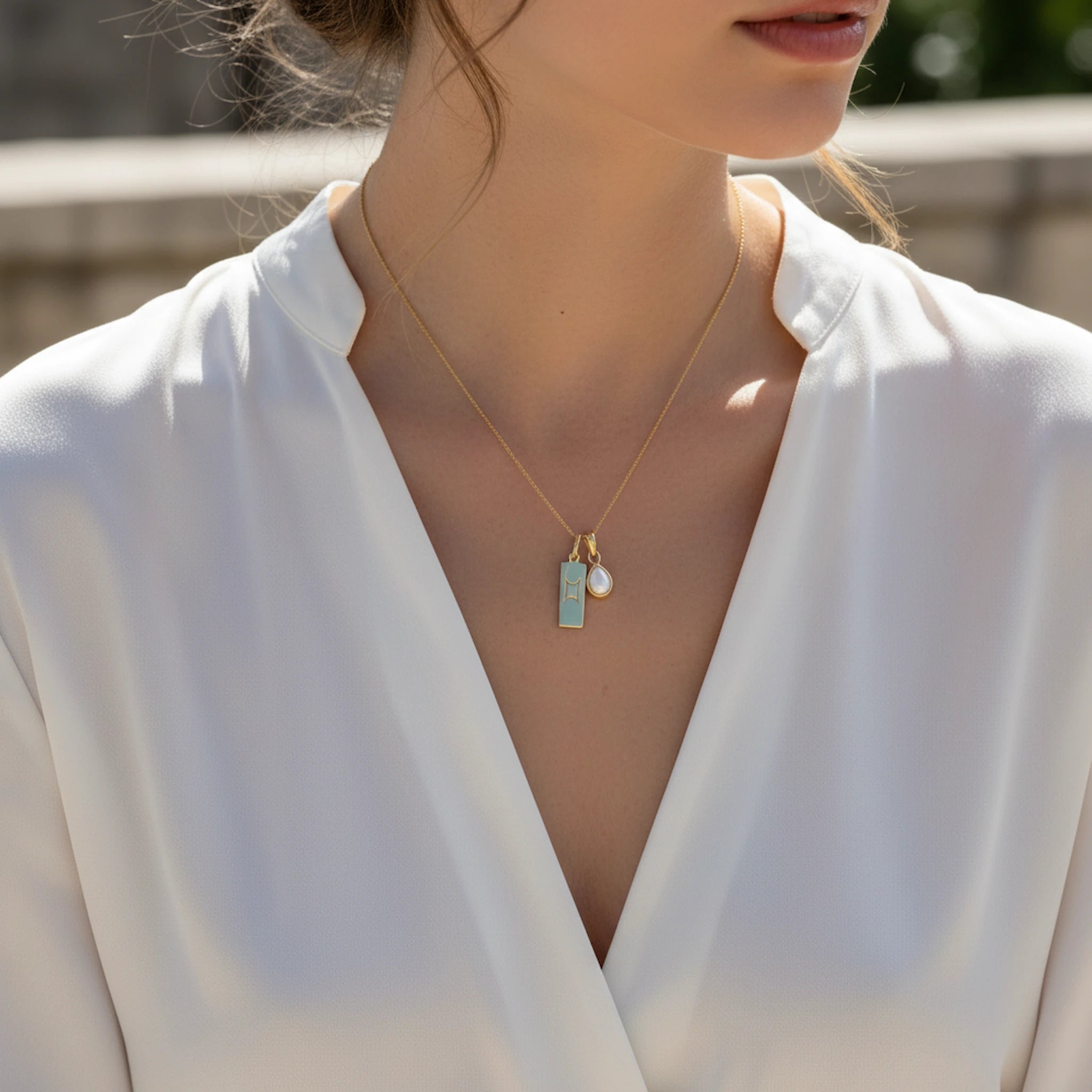 Woman wearing a gold necklace with a pendant and pearl on a blurred outdoor background