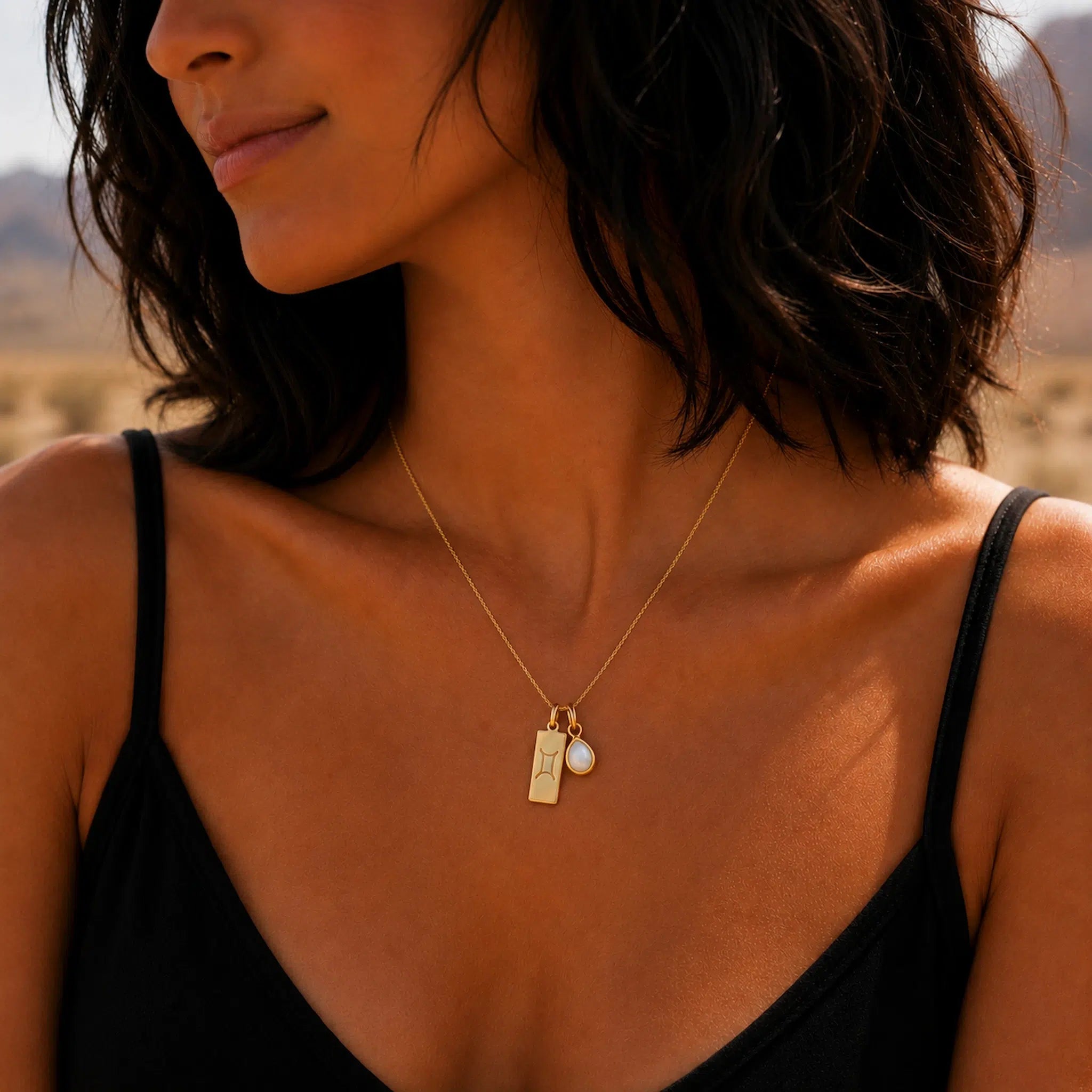 Close-up of a woman wearing a gold necklace with a tear drop june birthstone pearl pendant and a gemini zodiac line glyph pendant.