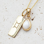 Gold necklace with a tear drop june birthstone pearl pendant with a gemini zodiac pendant on a light background