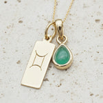 gold necklace with a May Birthstone emerald gemstone pendant and a Gemini Zodiac Star Sign pendant on a white background