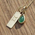 Gold necklace with a Gemini sign pendant and green emerald gemstone on a wooden surface