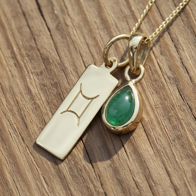 Gold necklace with a Gemini sign pendant and green emerald gemstone on a wooden surface