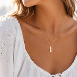 model wearing a dainty gold chain necklace with a rectangle pendant engraved with the gemini zodiac line glyph