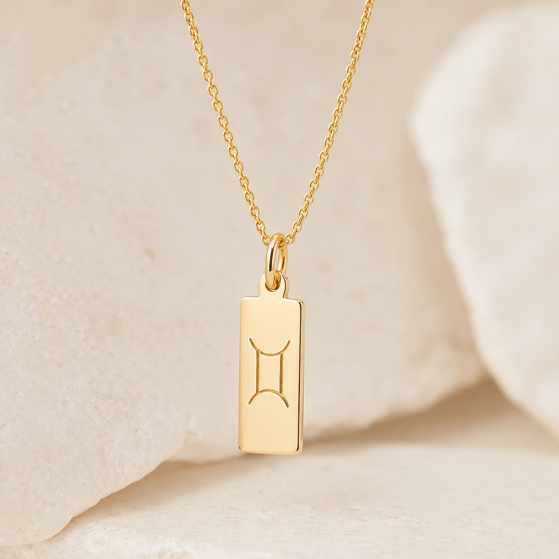gold fine chain necklace with a rectangle pendant engraved with the gemini zodiac line glyph symbol hanging.