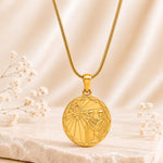 A gold pendant necklace featuring a gemini zodiac symbol, suspended from a gold chain against a soft beige satin background with small white flowers.