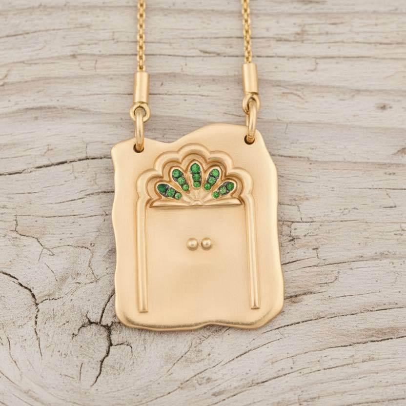 Gold necklace with a pendant featuring green gemstones on a wooden surface