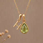 Gold Initial H Pendant and August birthstone Natural Peridot Necklace against a warm background