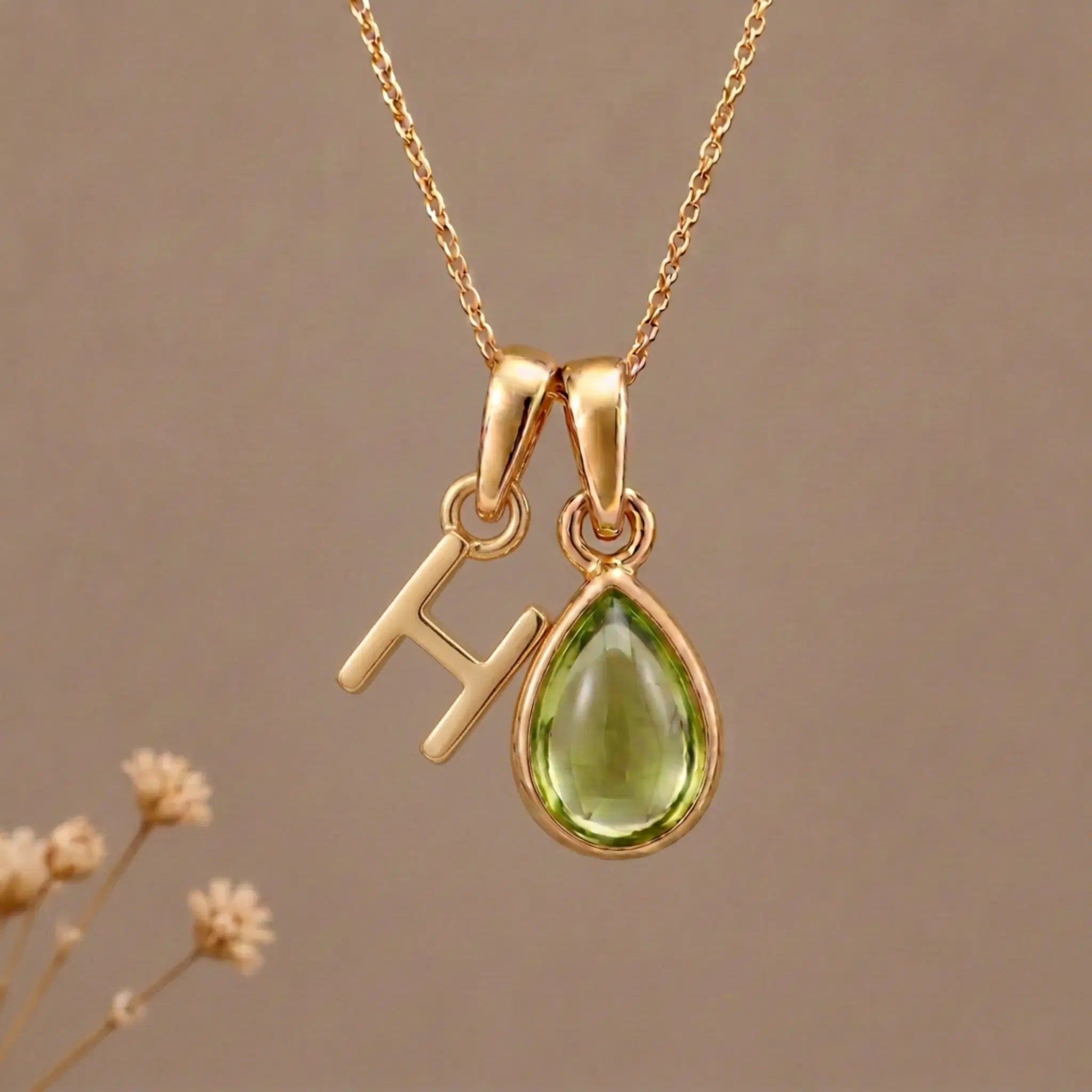 Gold Initial H Pendant and August birthstone Natural Peridot Necklace against a warm background