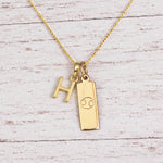 Gold Initial H Pendant and Cancer Zodiac Pendant Necklace on a fine gold chain against a light wooden background
