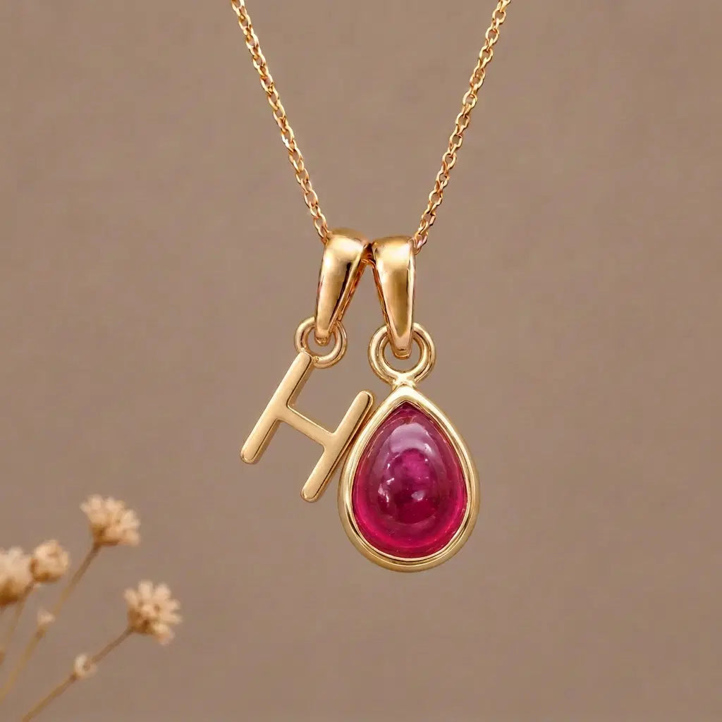 Gold Initial H Pendant and July birthstone Natural Ruby Necklace against a warm background