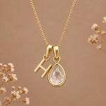 Gold initial H necklace with an April clear quartz teardrop on brown with dried flowers