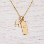 gold H initial and aquarius zodiac necklace on fine gold chain against a light wooden background
