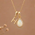 Gold Initial H Pendant and October birthstone Natural Opal Necklace against a warm background