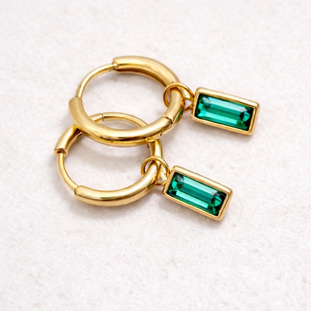 Gold hoop earring with green gemstones on a gray background