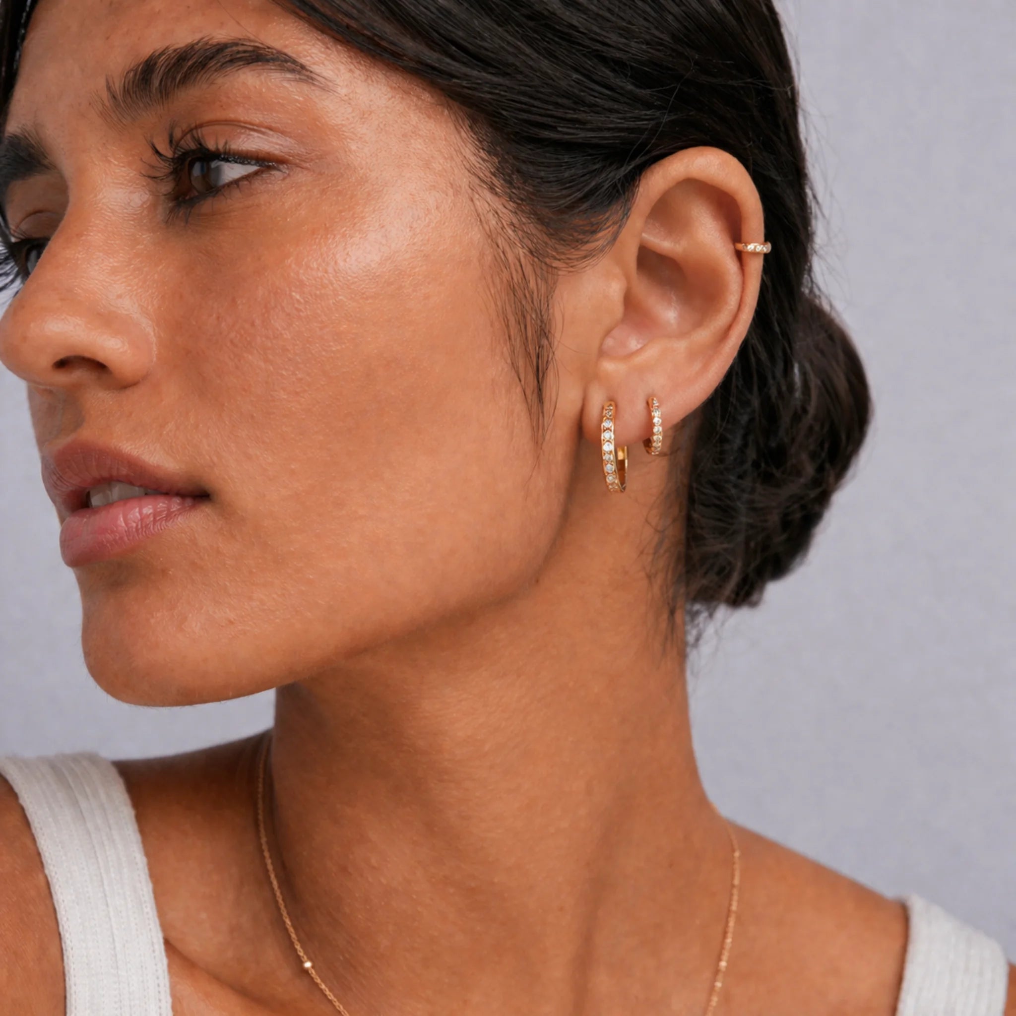 Model wearing a stack of gold pavé huggie hoop earrings in double lobe piercings with a matching gold helix hoop