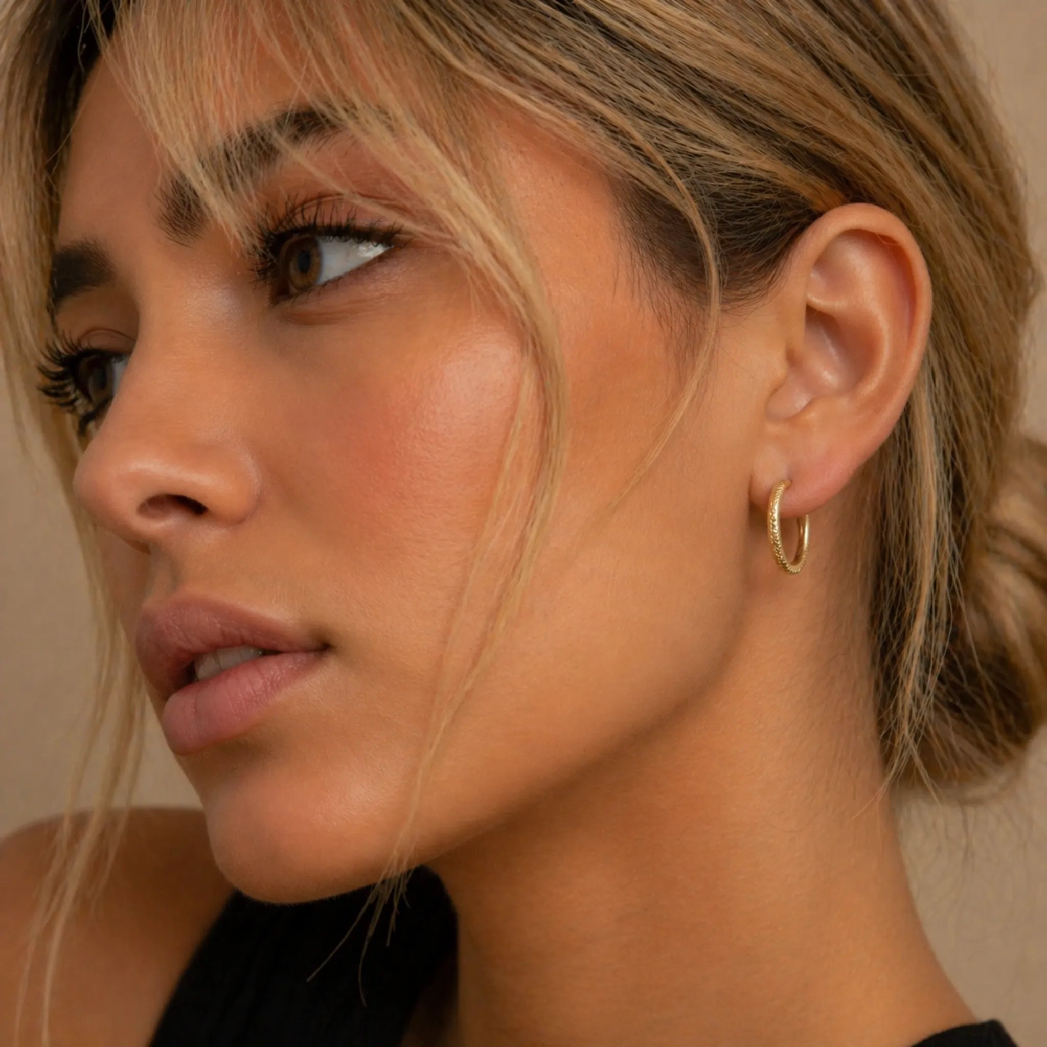 Close-up of a woman wearing a stainless steel waterproof gold hoop earring against a neutral background