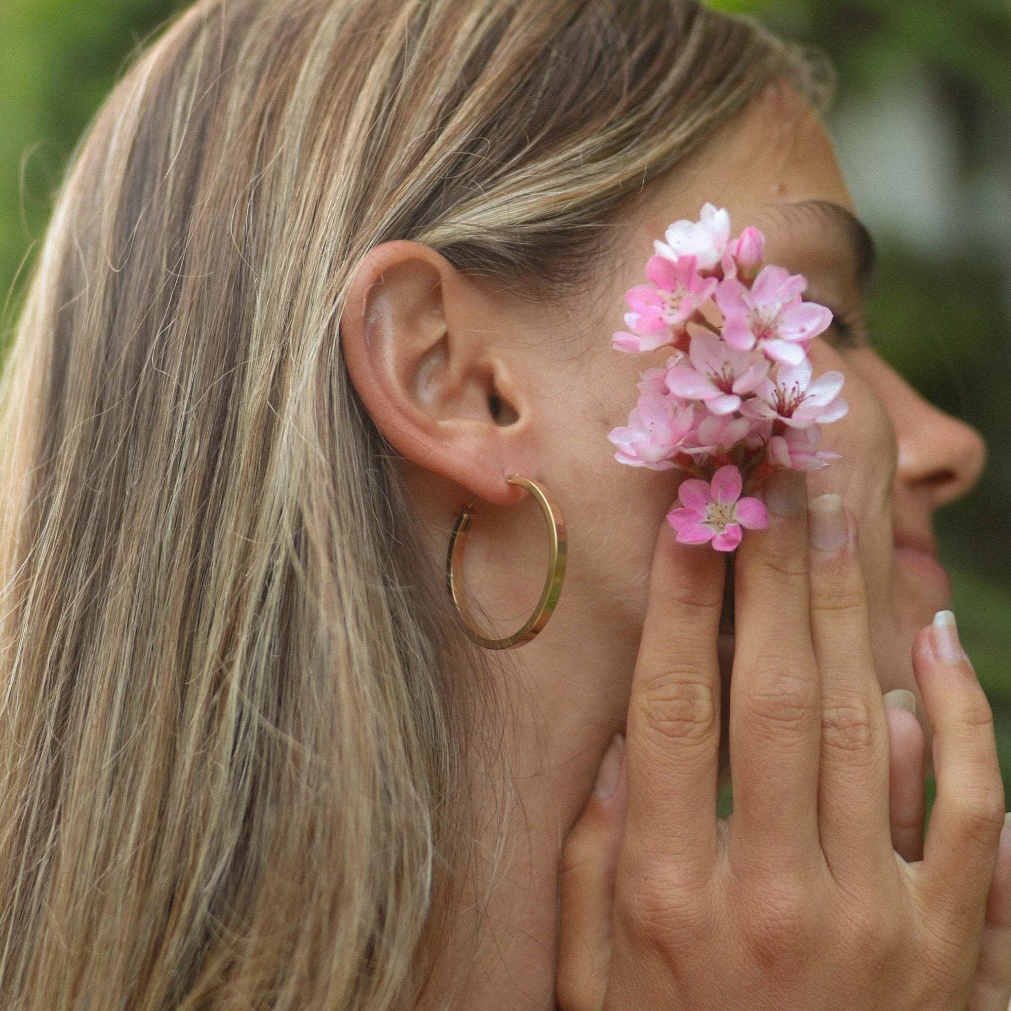 Woman wearing stainless steel waterproof classic polished gold hoop Earrings and holding pink flowers