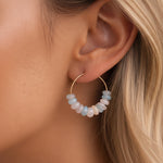 Close-up of an ear wearing a gold hoop earring with multicolored beads.