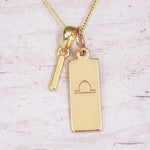 Gold initial and Libra zodiac necklace with a letter I charm and engraved bar pendant on whitewashed wood