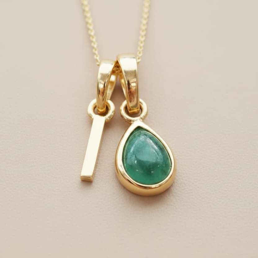 Gold necklace with a green teardrop pendant on a beige background