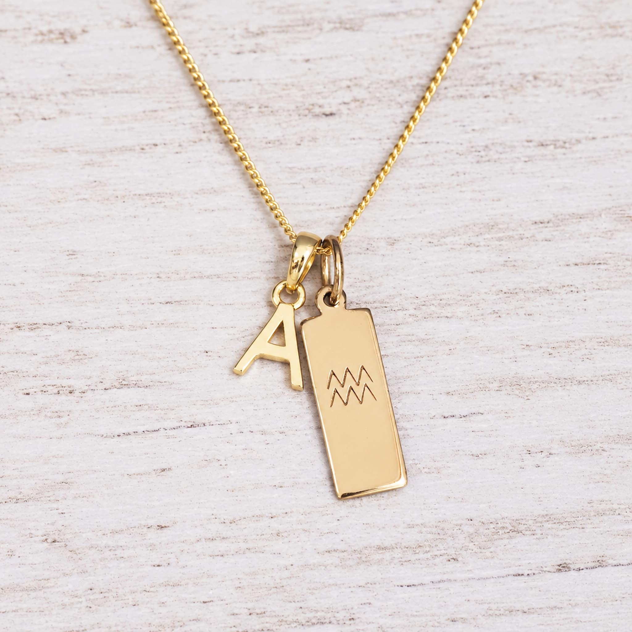 Gold Initial and Aquarius Zodiac Necklace with letter A pendant on light wood