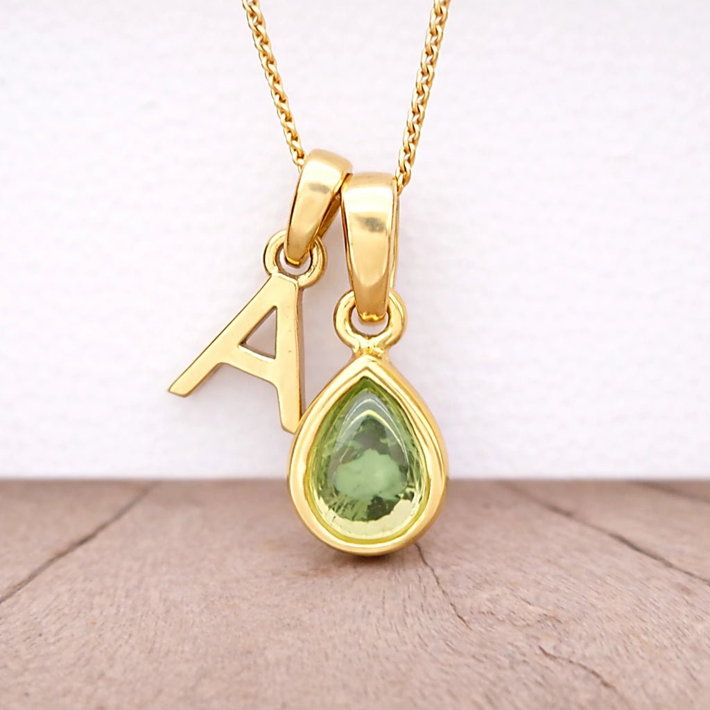 Gold necklace with a green teardrop pendant and letter 'A' charm on a light background