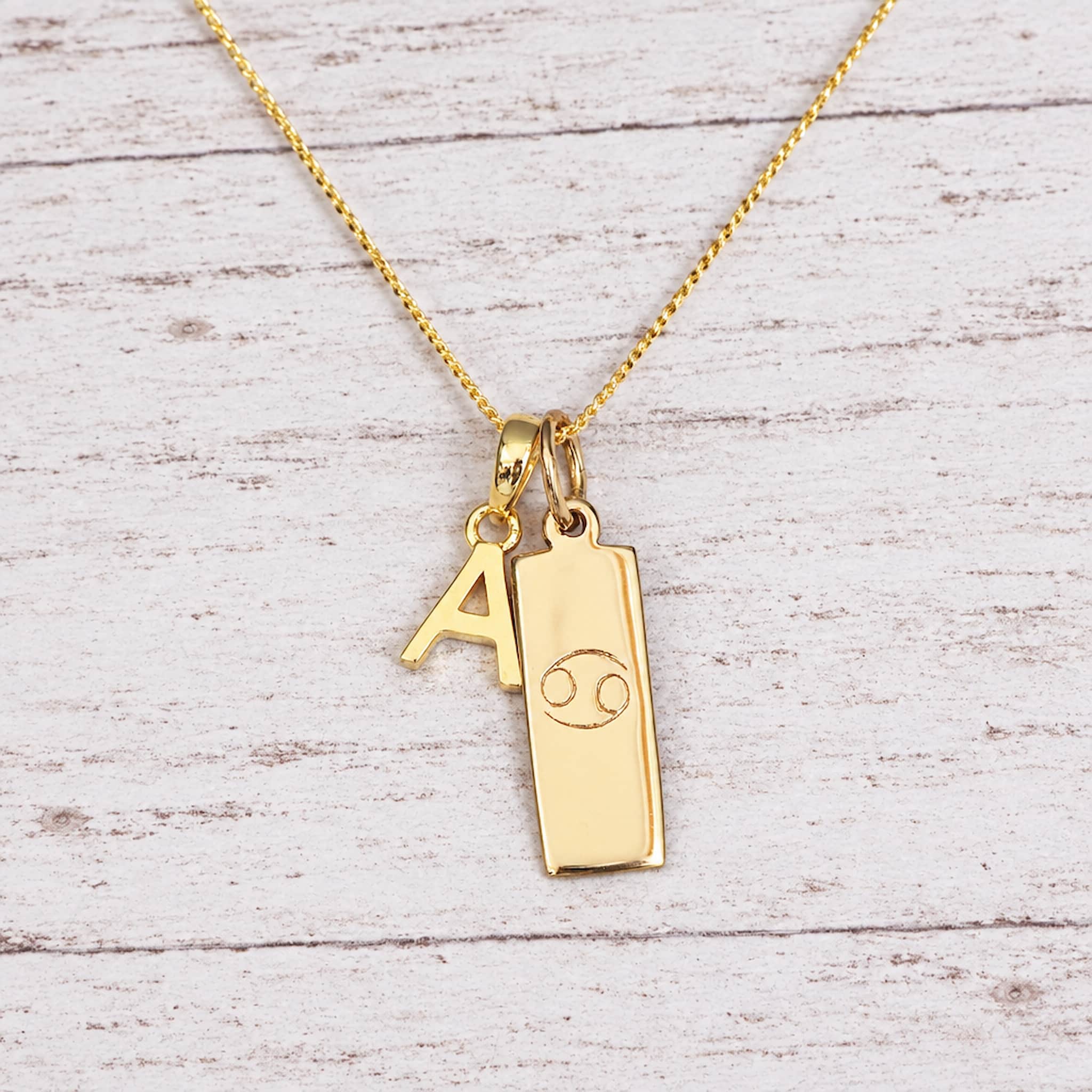 Gold Initial and Cancer Zodiac Necklace with letter A pendant on light wood