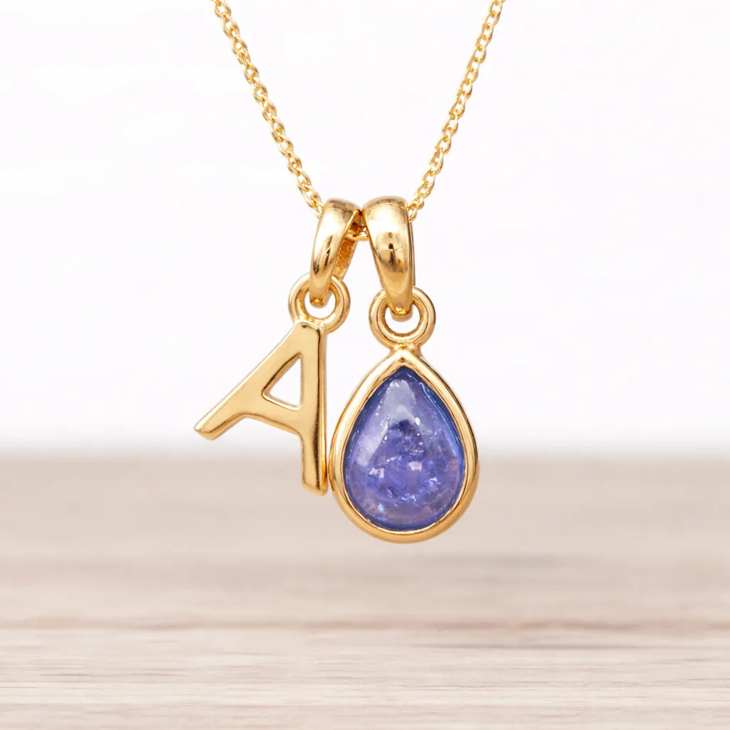 Gold necklace with a teardrop-shaped tanzanite pendant and an 'A' initial.