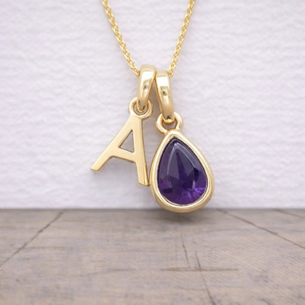 Gold necklace with a purple teardrop pendant and letter 'A' charm on a light background
