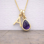Gold necklace with a purple teardrop pendant and letter 'A' charm on a light background