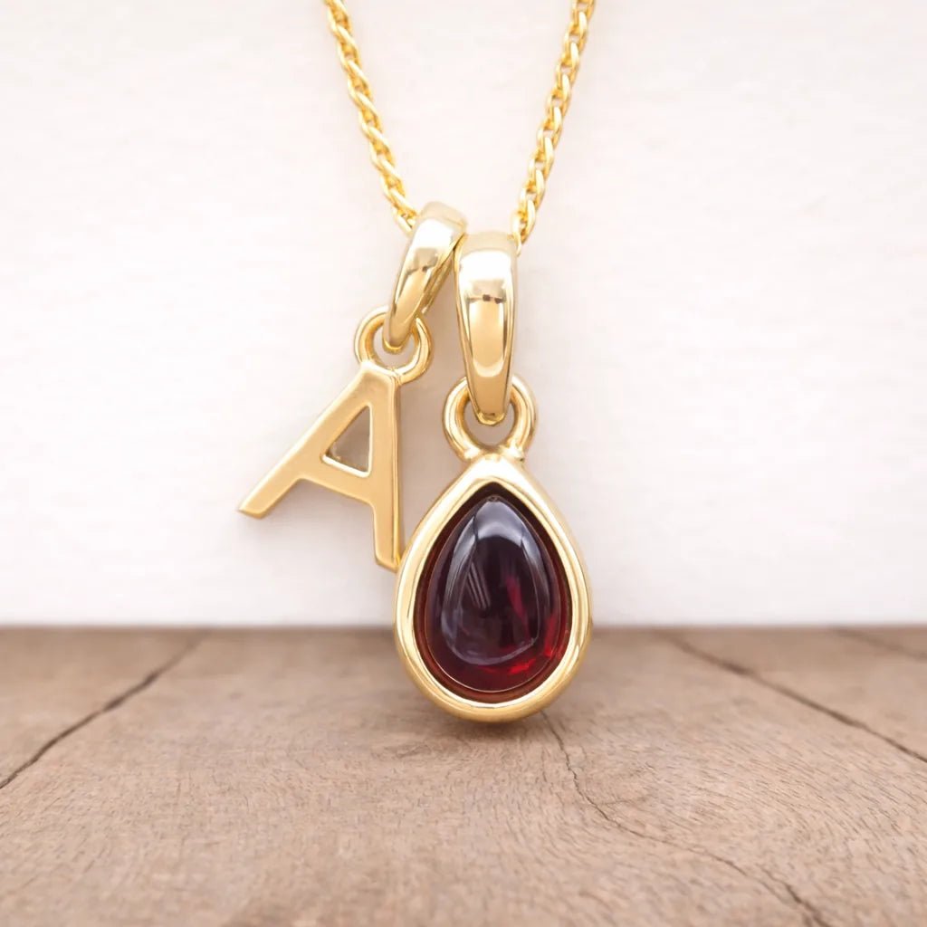 gold a initial and january birthstone garnet necklace hanging above a wooden surface