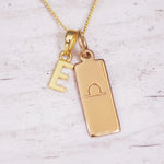 Gold necklace with 'E' pendant and libra zodiac sign on a light background
