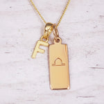 Gold necklace with 'F' pendant and libra zodiac sign on a light background