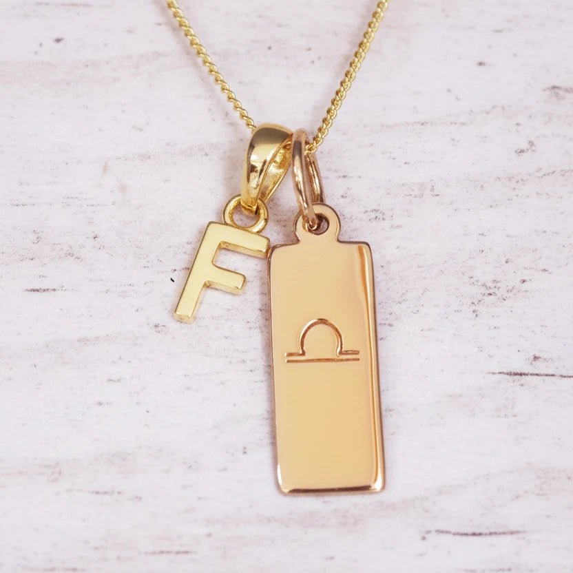 Gold necklace with 'F' pendant and libra zodiac sign on a light background
