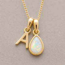 Gold October birthstone necklace with a pear-shaped natural opal pendant and letter 'A' charm with a light background.