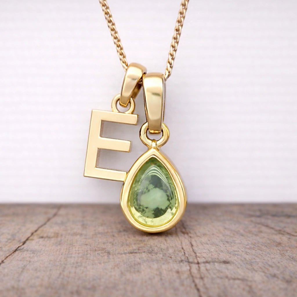 Close-up of personalised gold-plated E initial charm and light green pear-shaped peridot pendant on a fine chain, August birthstone necklace