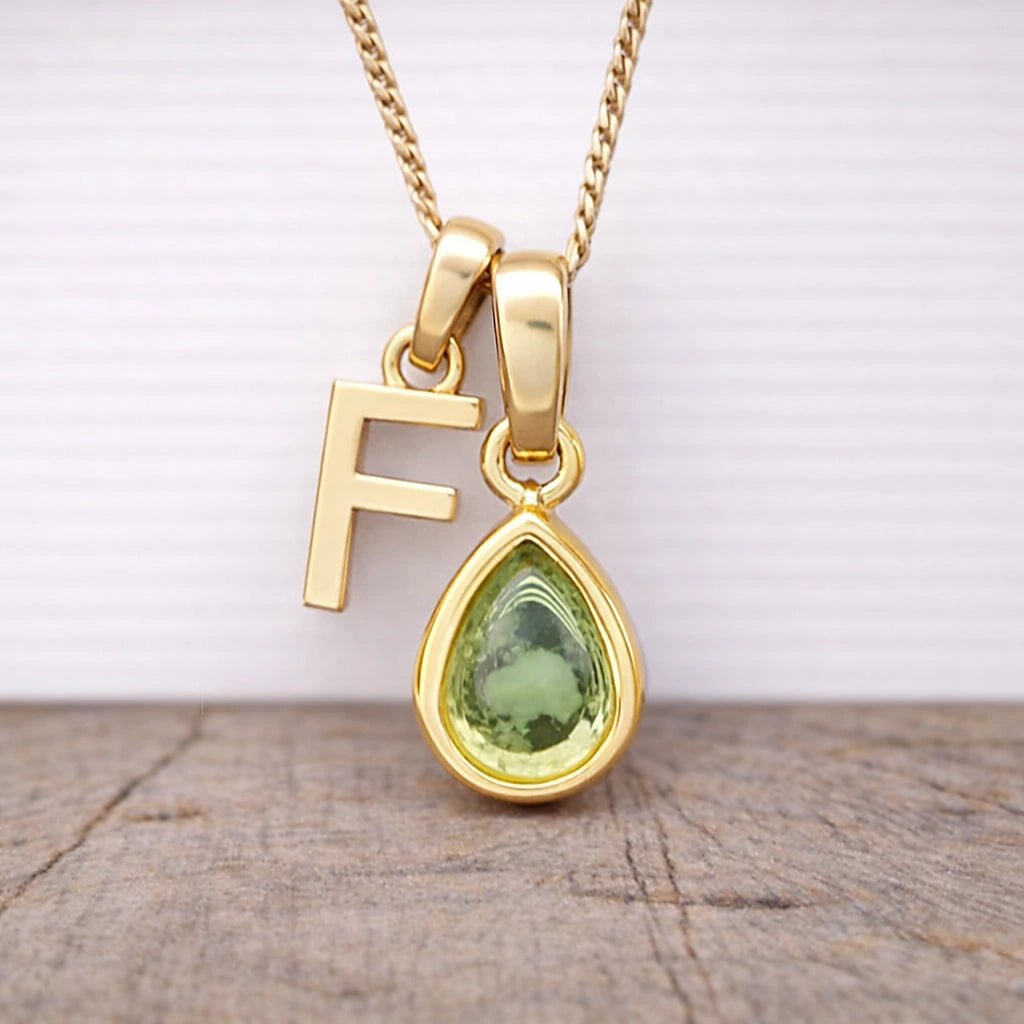 Close-up of personalised gold-plated F initial charm and light green pear-shaped peridot pendant on a fine chain, August birthstone necklace
